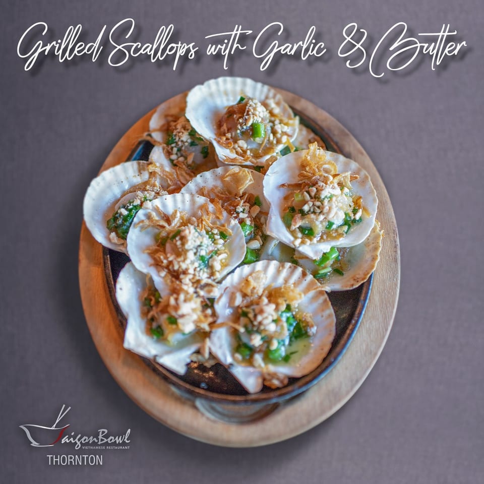 A platter of Vietnamese grilled scallops with garlic, butter, peanuts, and green onions in their shells.