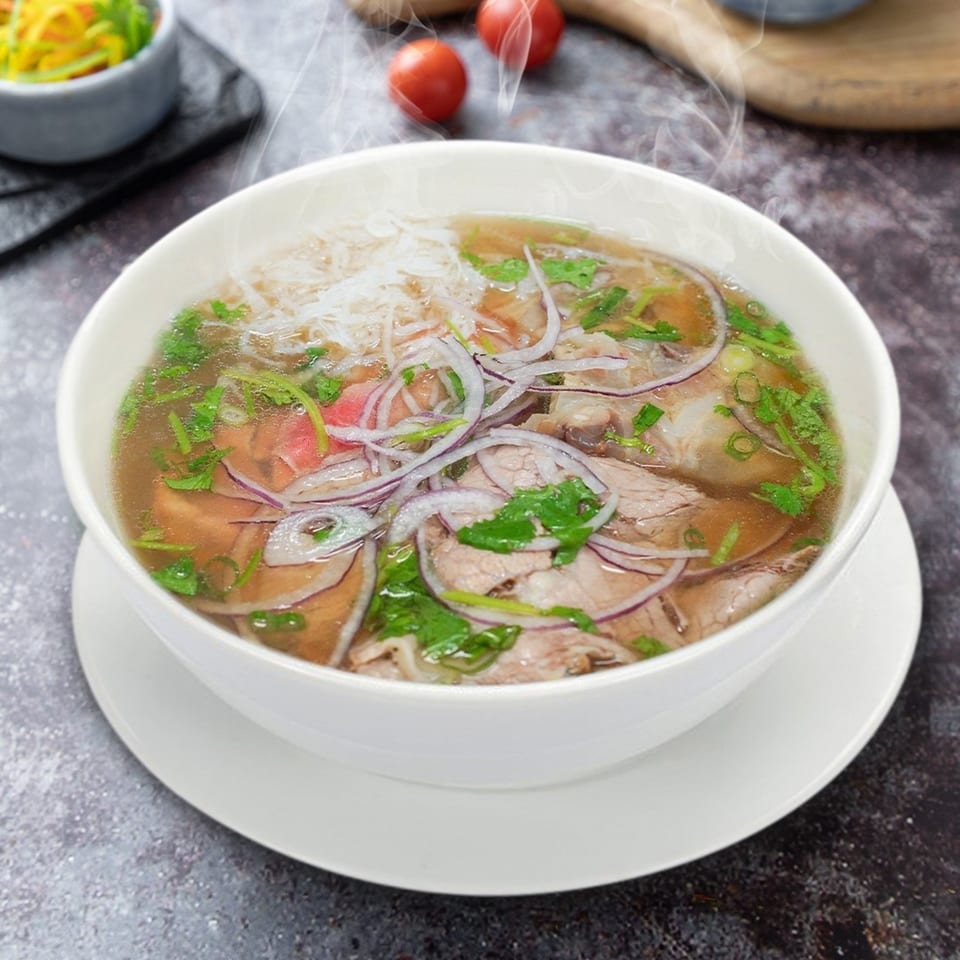 Steaming bowl of Vietnamese pho with beef, noodles, red onions, and fresh herbs.